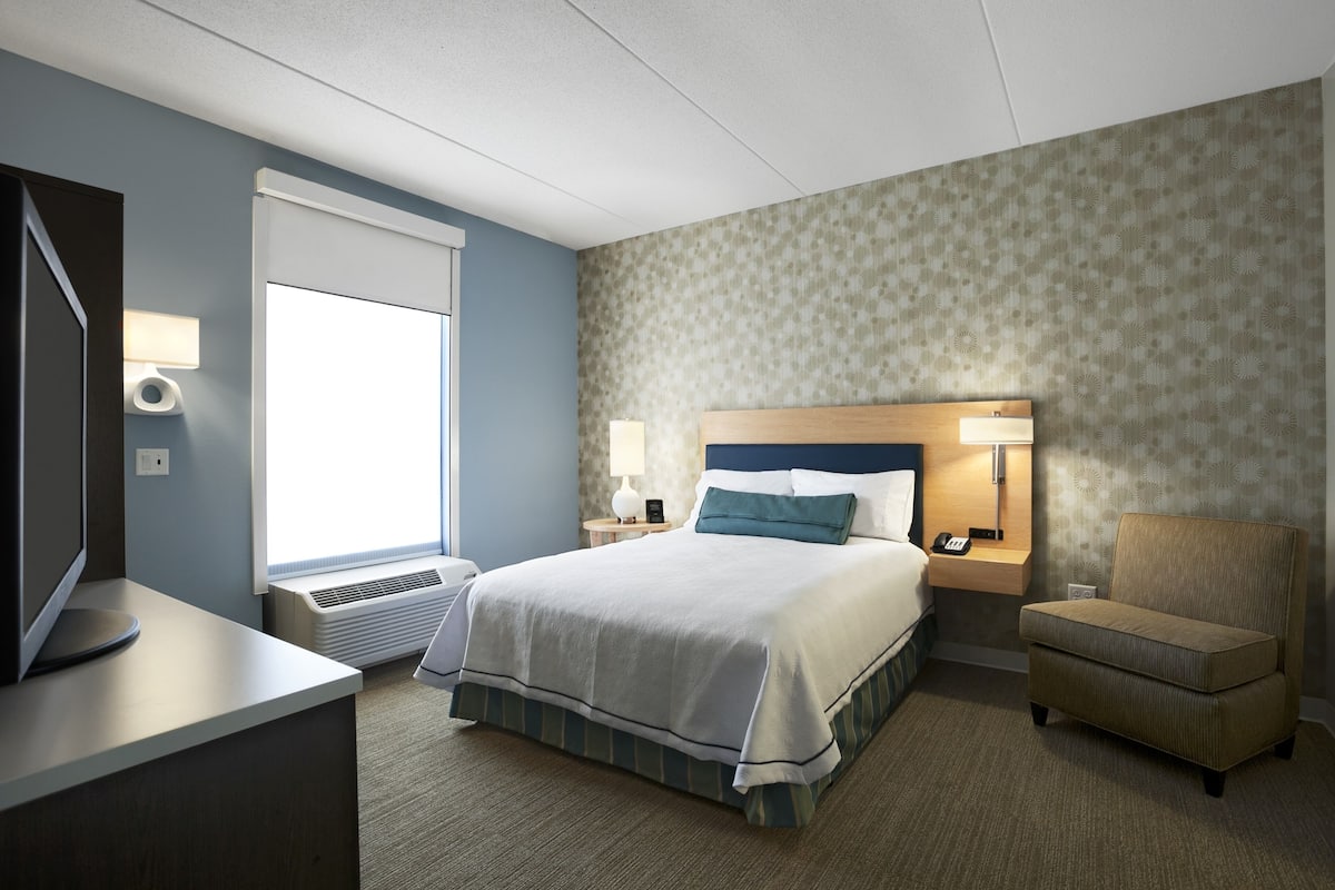 Ein Hotelzimmer mit Bett, Fernseher, Schreibtisch, Stuhl und Fenster.