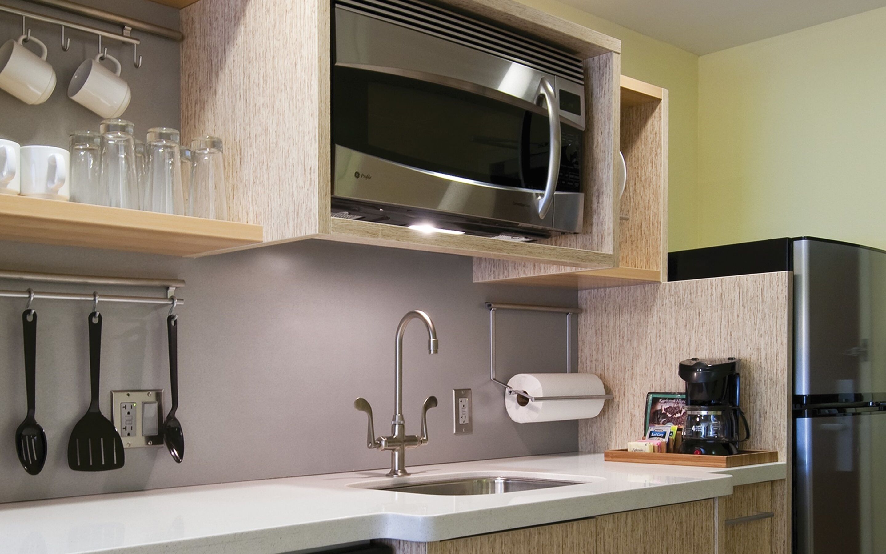 A kitchen with a stainless steel refrigerator, a built-in microwave, a sink, and various utensils hanging on the wall.