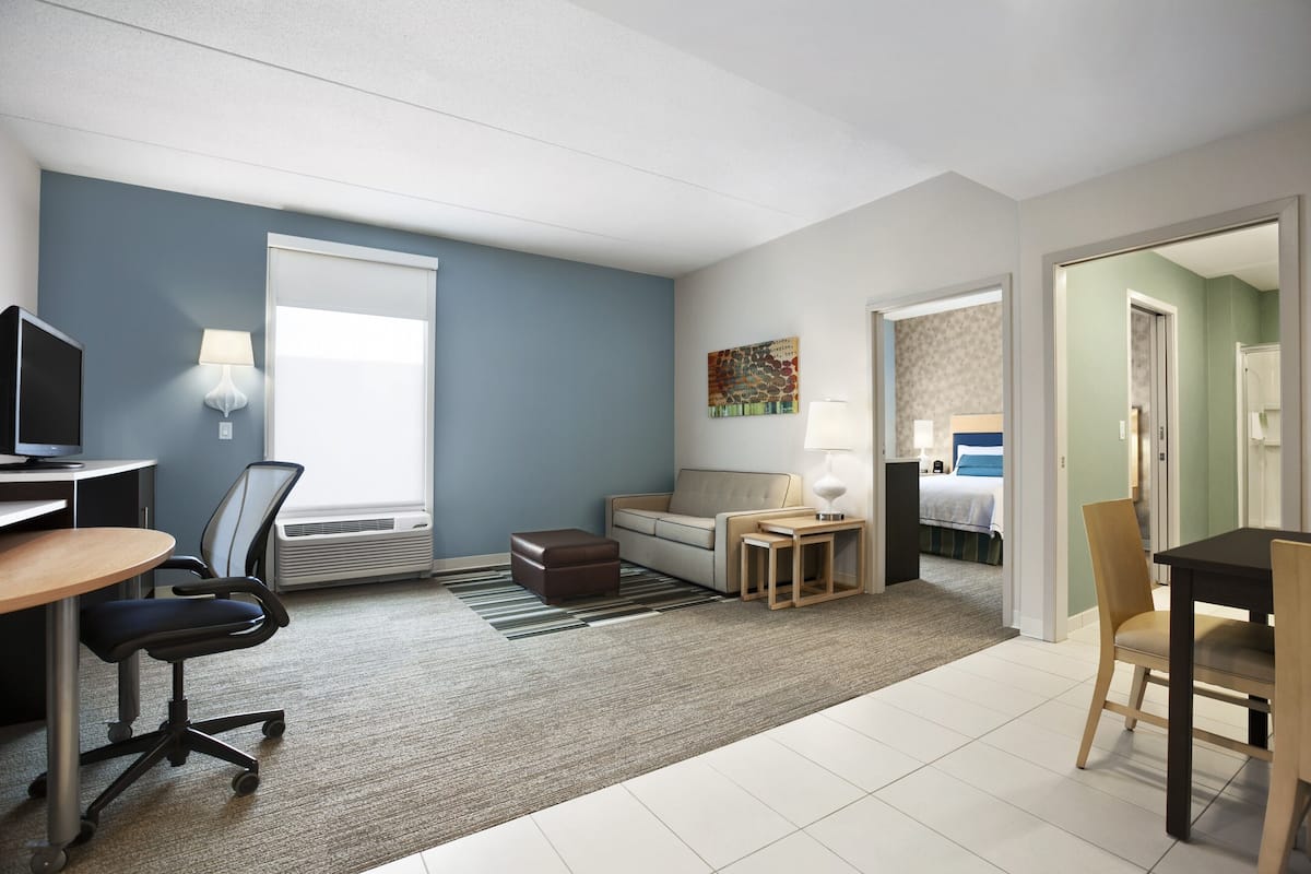 Ein modernes Hotelzimmer mit Schreibtisch, Bürostuhl, Sofa und Esstisch.