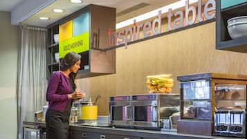 A breakfast bar with a sign reading "inspired table," a microwave, toaster, and a bowl of fruit.