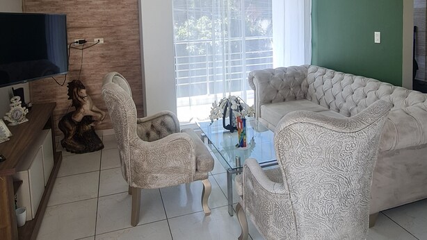 A living room with a sofa, two patterned chairs, a glass coffee table, a TV, and a wooden cabinet. - Lindo y Acogedor Apartamento Cerca de Todo (Barranquilla)