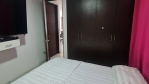 A bedroom with a bed, a wardrobe, a TV, and a door leading to another room. - Lindo y Acogedor Apartamento Cerca de Todo (Barranquilla)