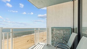 Un balcón con vista a la playa, un muro con diseño y dos sillas.