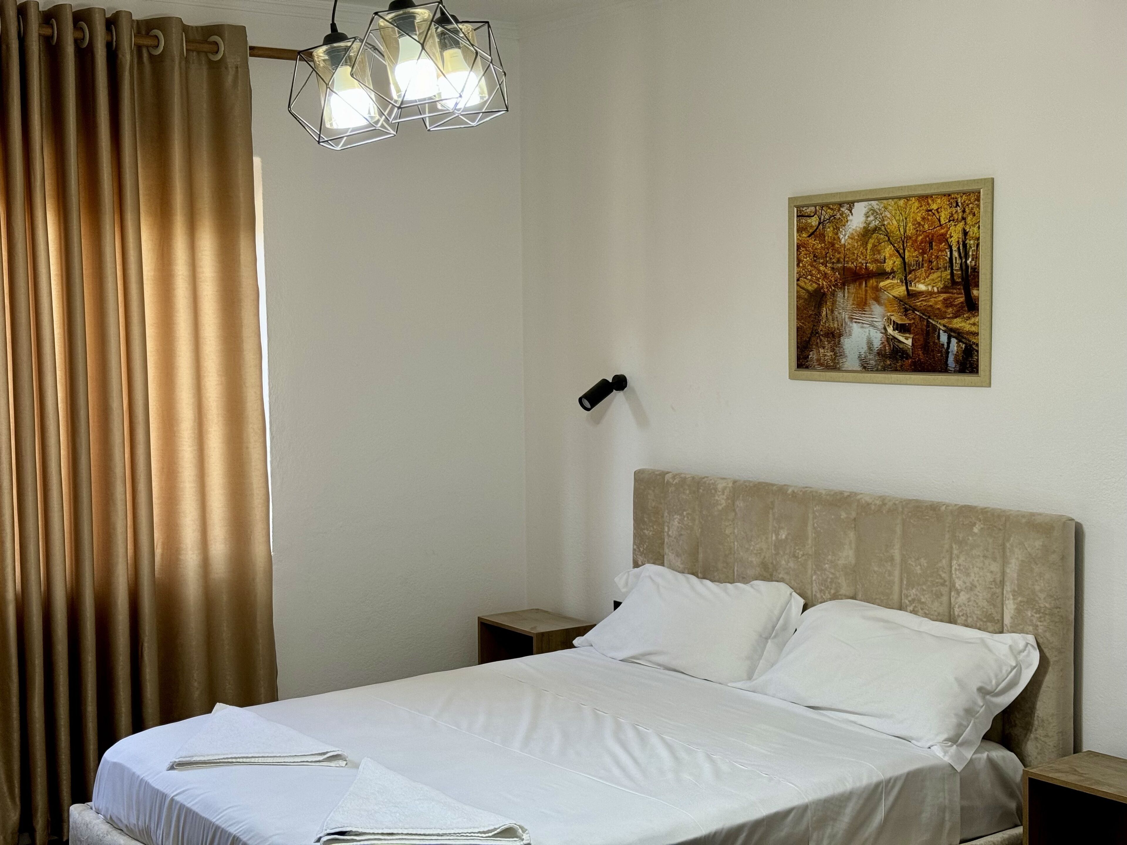 A hotel room with a bed, a painting of a landscape, and a geometric light fixture.