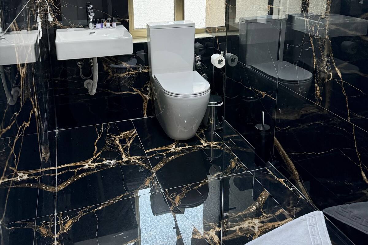 A modern bathroom with a black marble floor, a white toilet, and a large mirror above the sink.