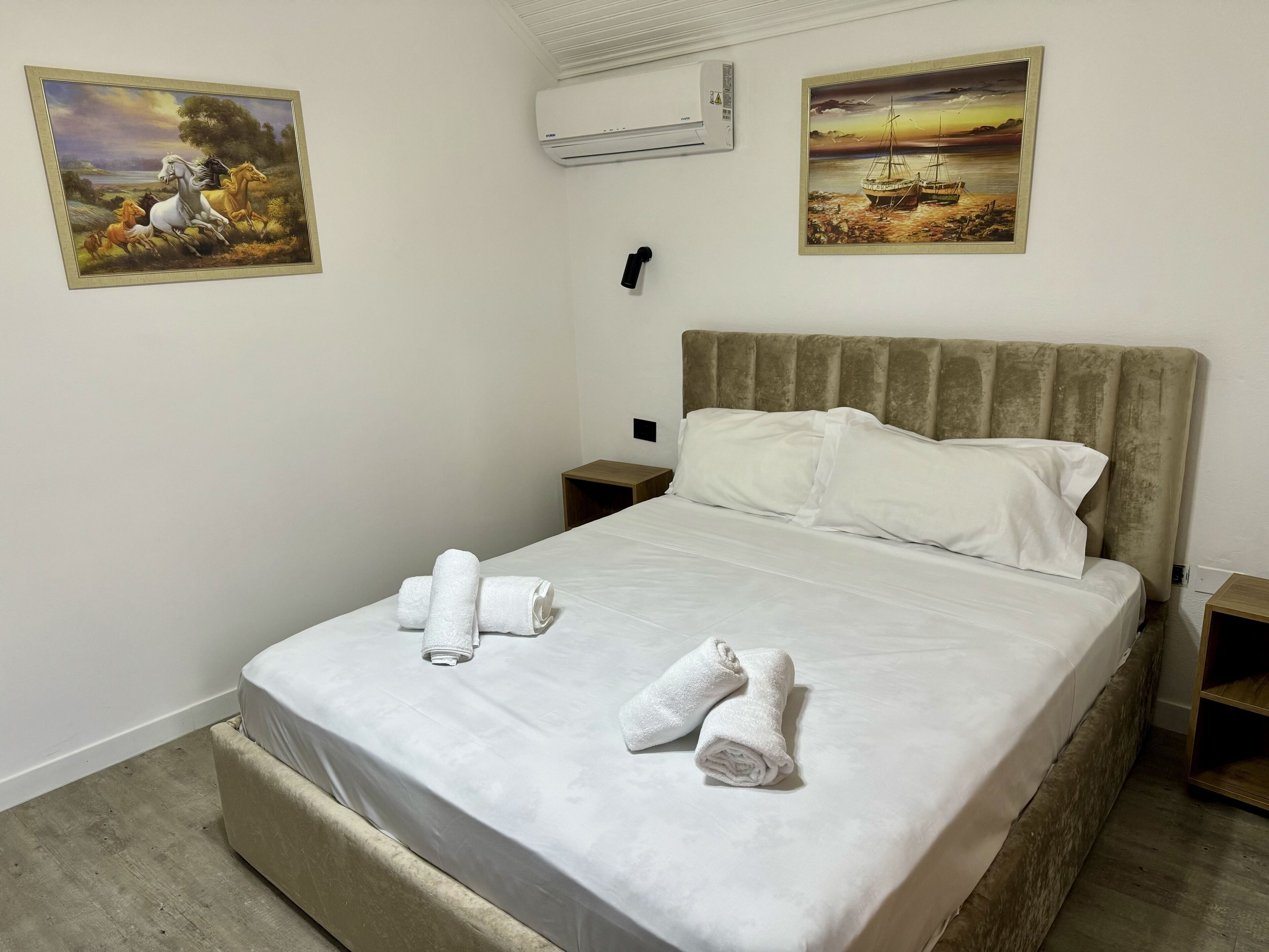 A neatly made bed with white linens and towels, a headboard, and two paintings on the walls.
