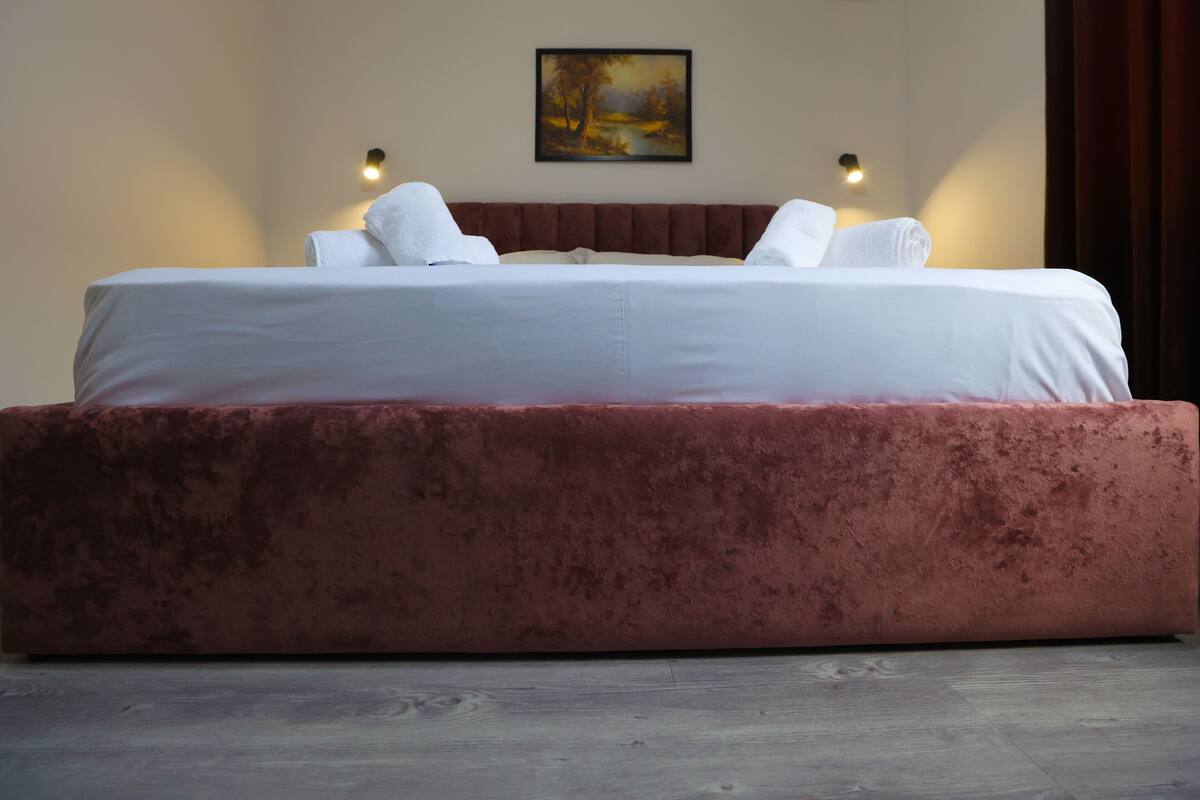 A large bed with a red upholstered headboard, white linens, and two wall-mounted reading lights.