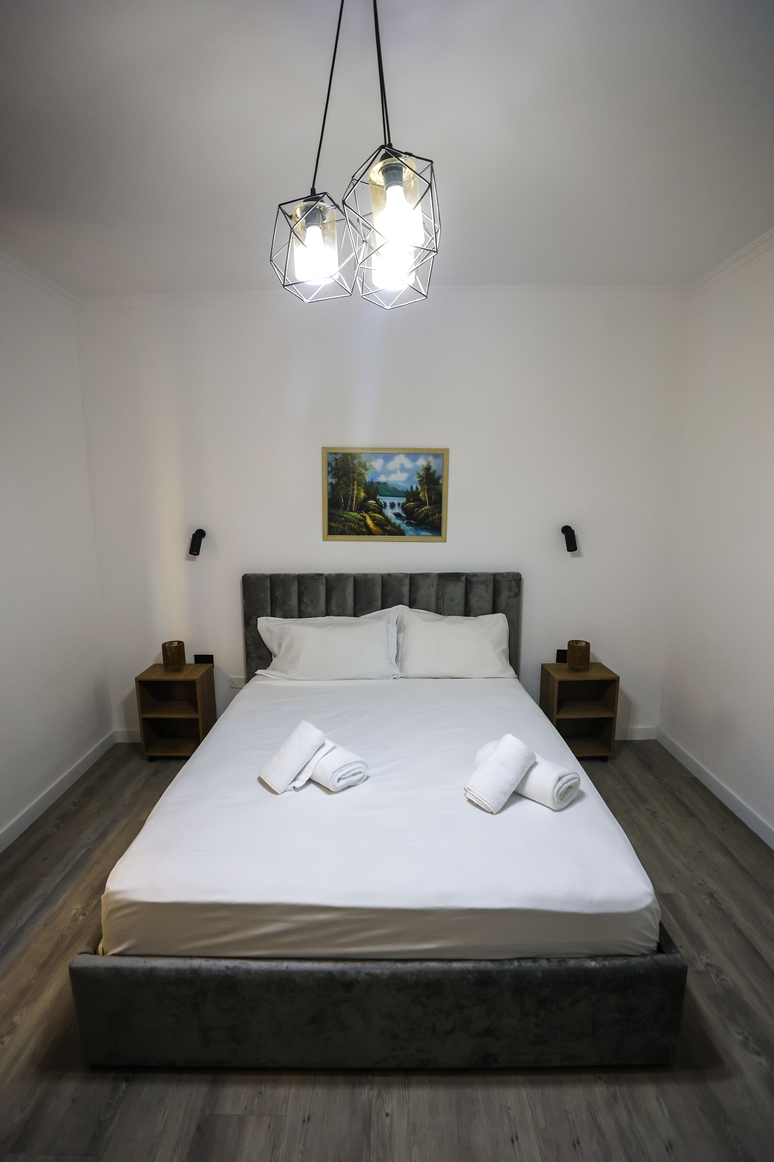 A neatly made bed with white linens, a grey upholstered headboard, and two bedside tables with lamps.