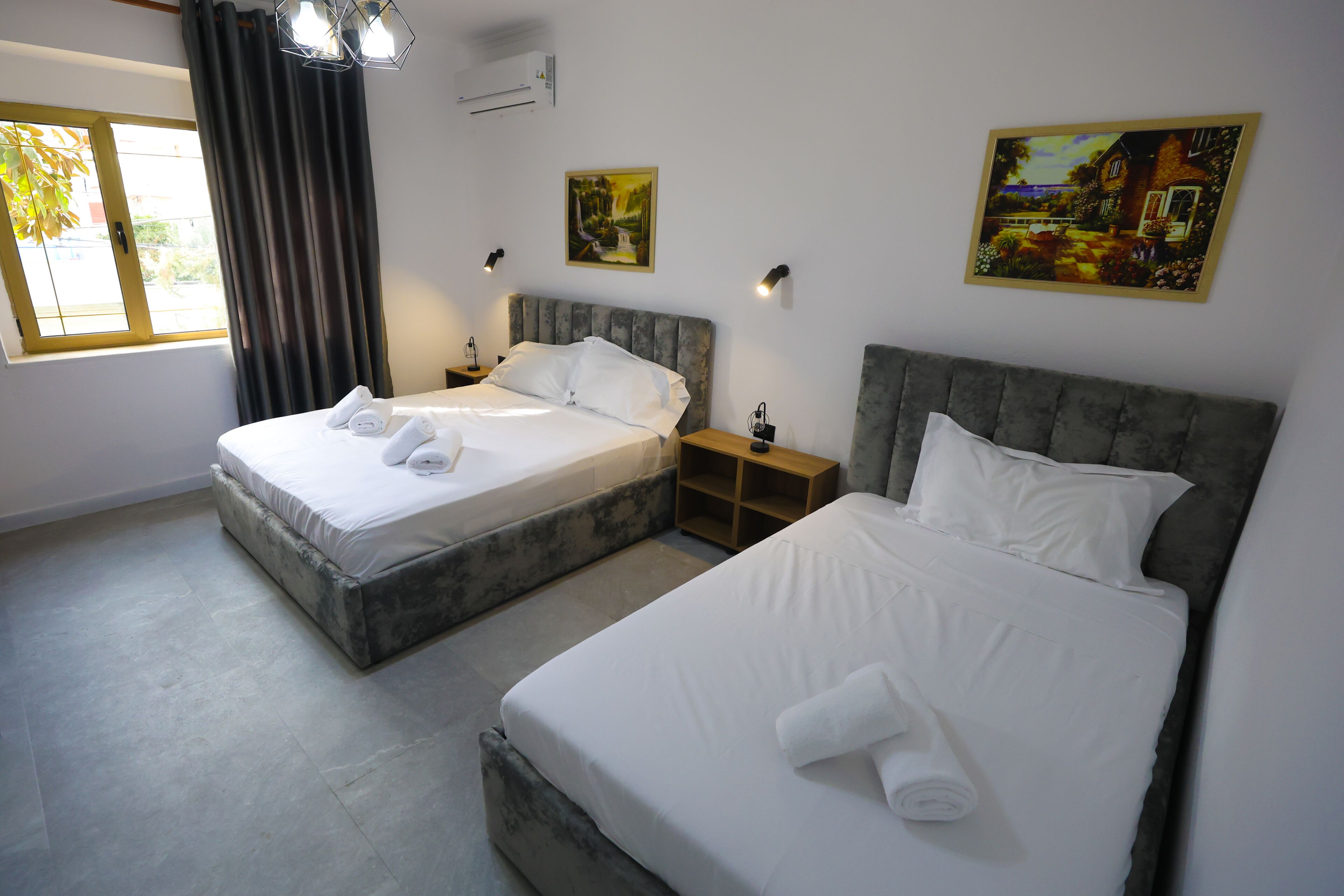 Une chambre d’hôtel avec deux lits, une fenêtre avec des rideaux et des œuvres d’art accrochées aux murs.