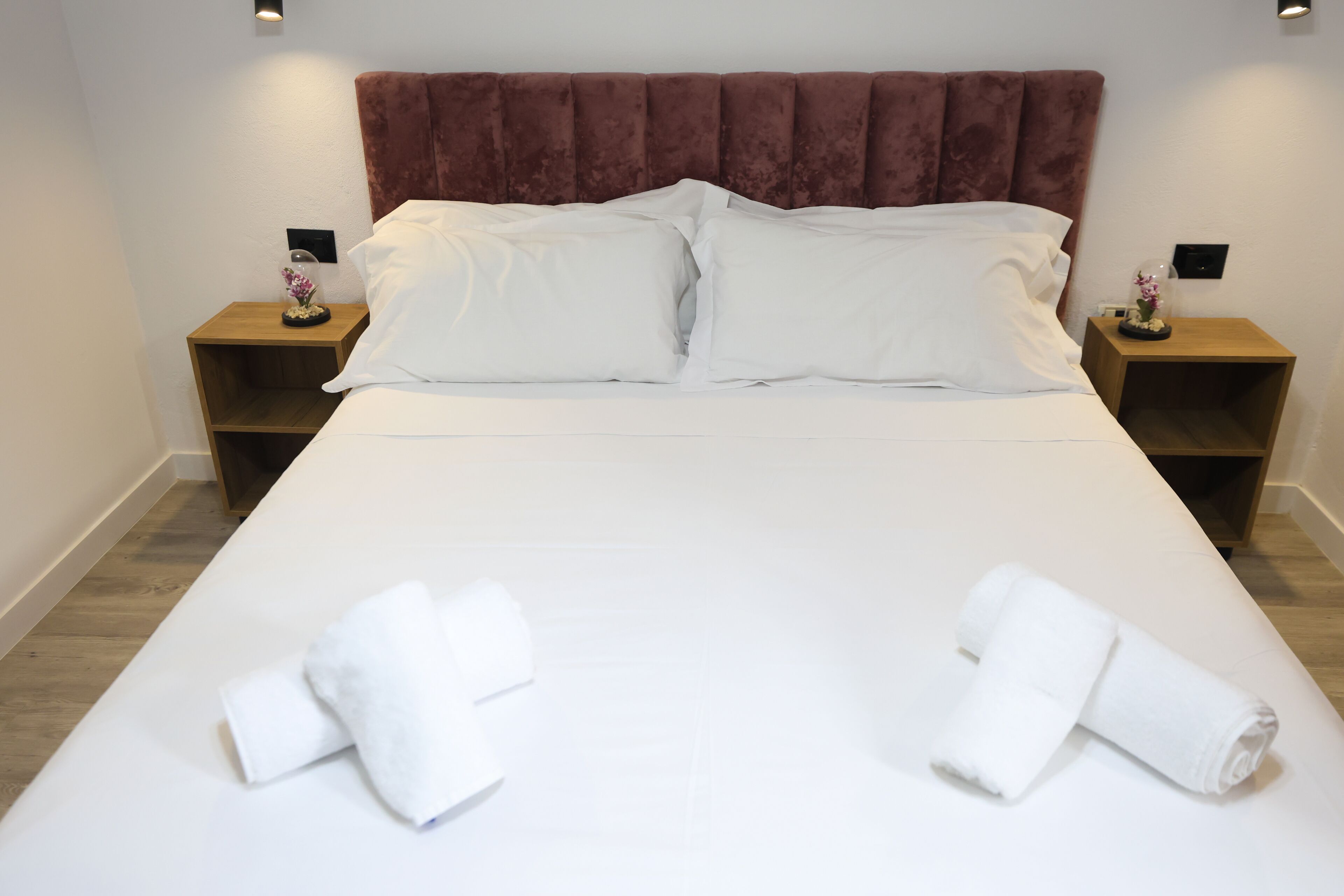 A neatly made bed with white linens, two pillows, and two rolled towels on the bed.