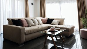 Ein modernes Wohnzimmer mit einem beigen Sofa, einem Glastisch und transparenten Vorhängen.