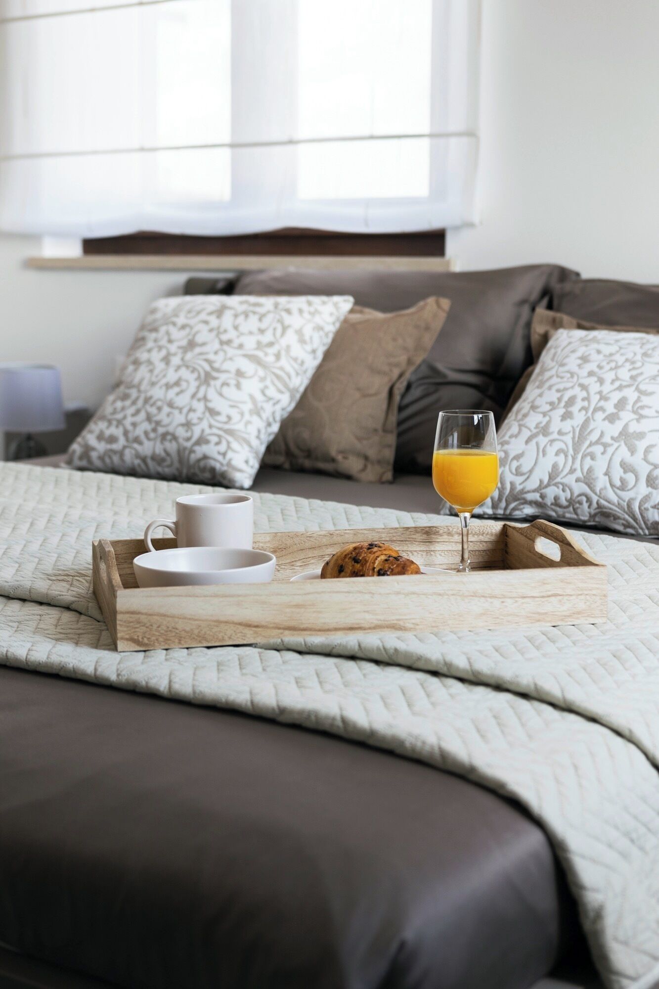 A neatly made bed with a tray of breakfast items including croissants, coffee cups, and orange juice.