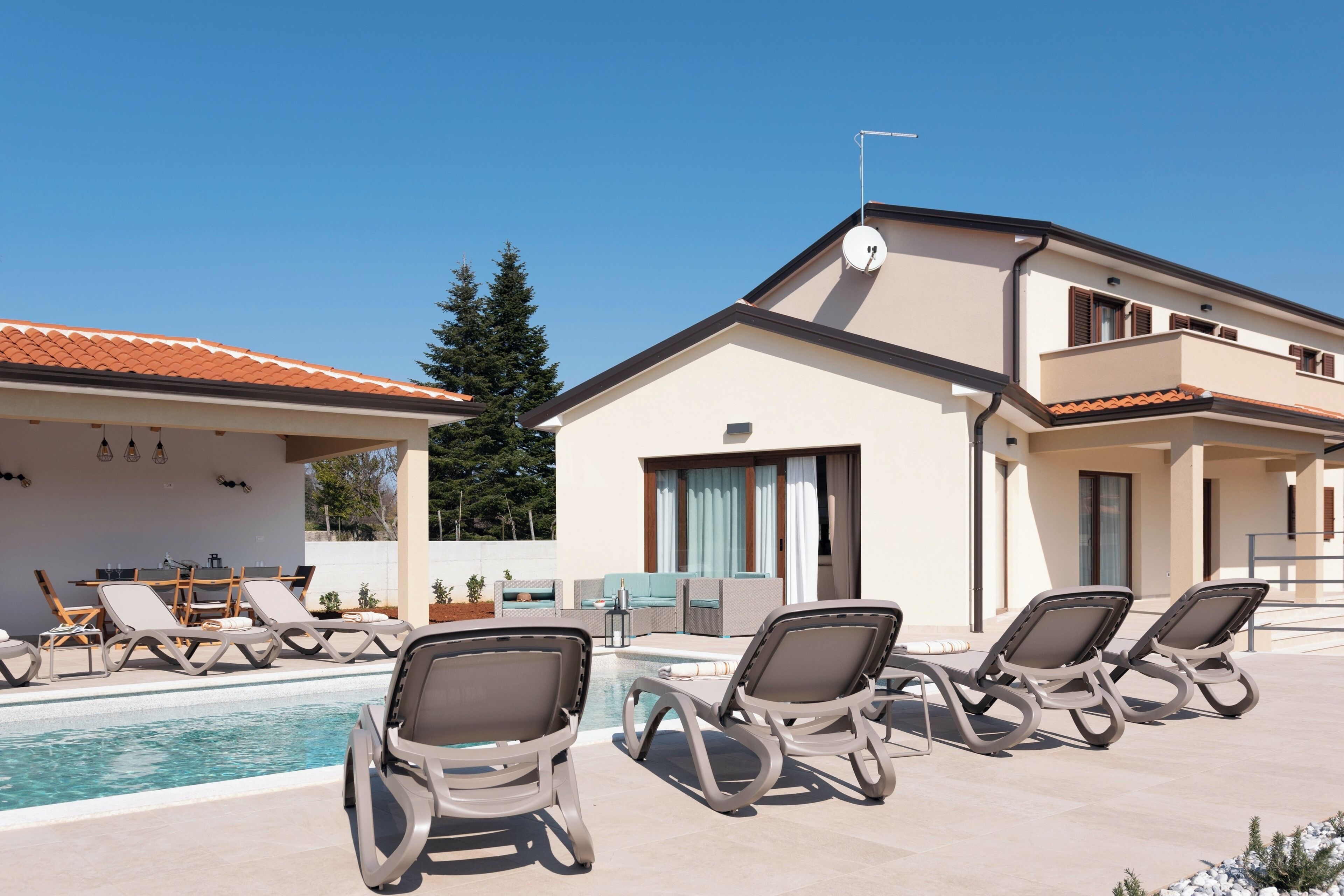A modern building with a pool area, including lounge chairs and a dining setup.