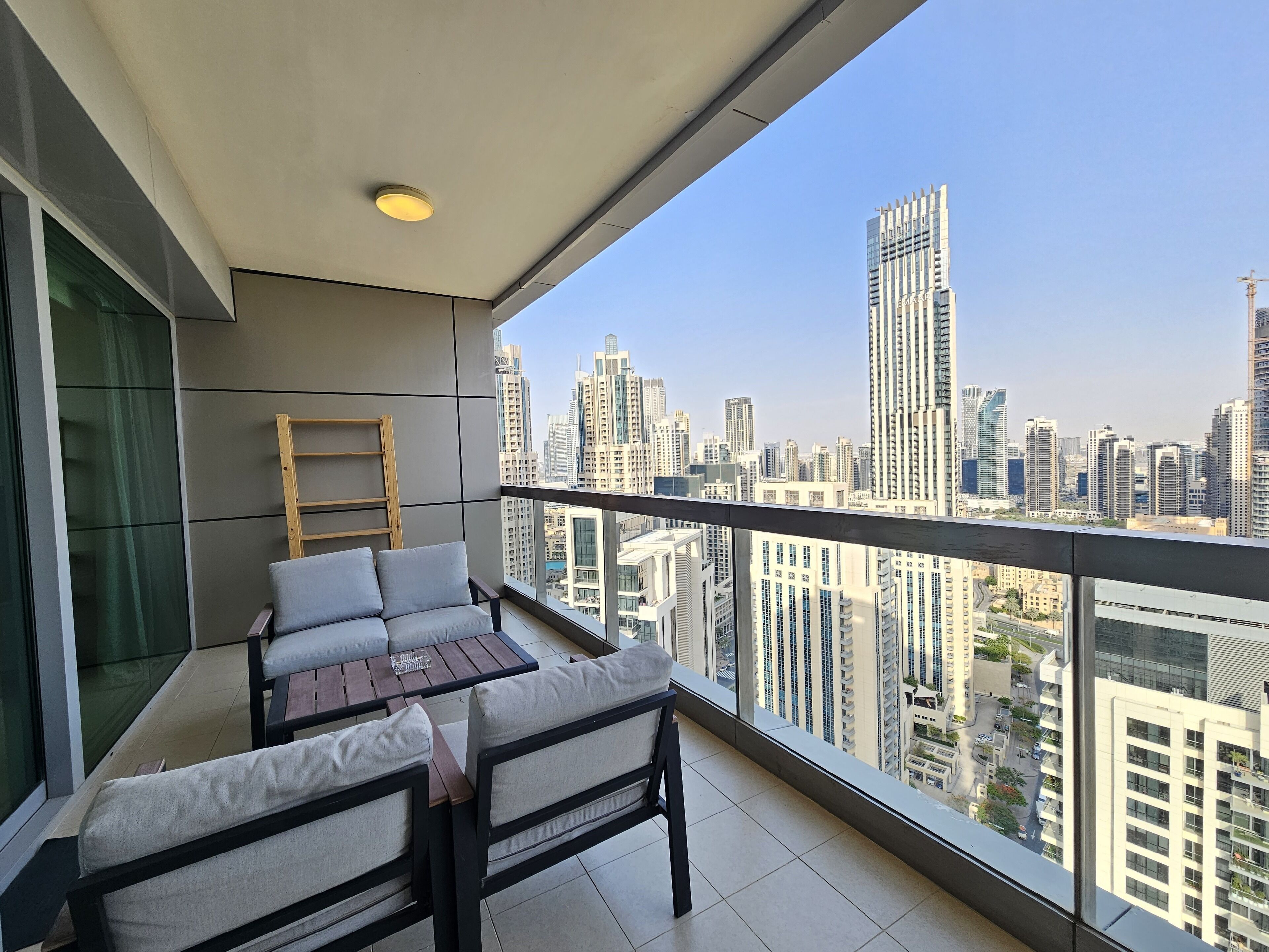 A balcony with a sofa and table, a wooden ladder, and a city view.