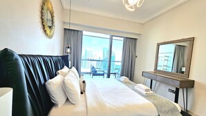 A hotel room with a large bed, a desk, a chair, and a view of the city. - Vacay Lettings - 8 Boulevard Walk (Dubai)
