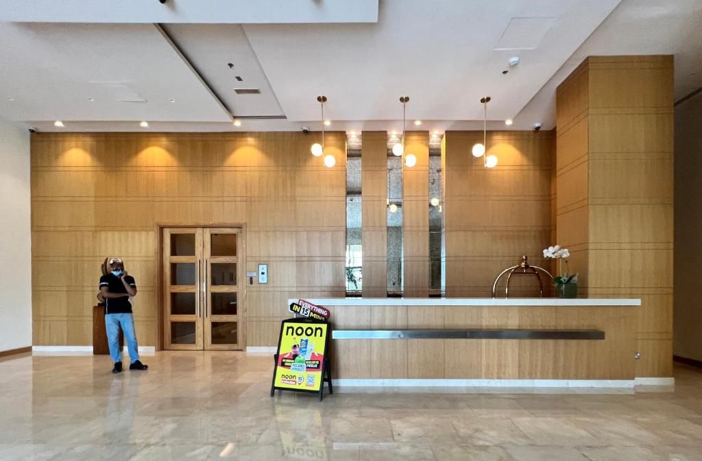 A hotel reception area with a wooden reception desk, a man standing by the door, and a sign indicating 'noon' services.