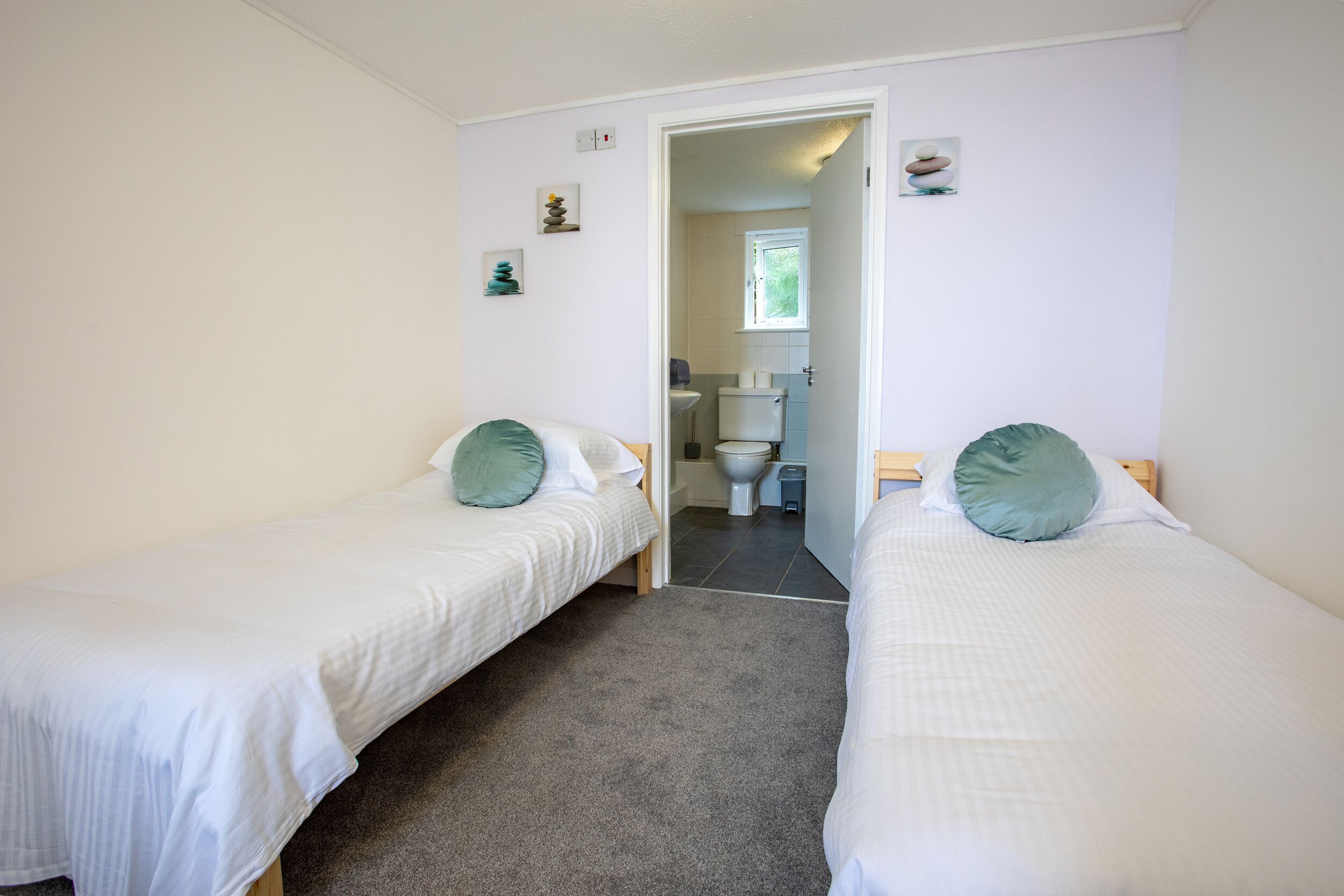 Ein Zimmer mit zwei Einzelbetten, einem kleinen Fenster und Blick ins Bad.