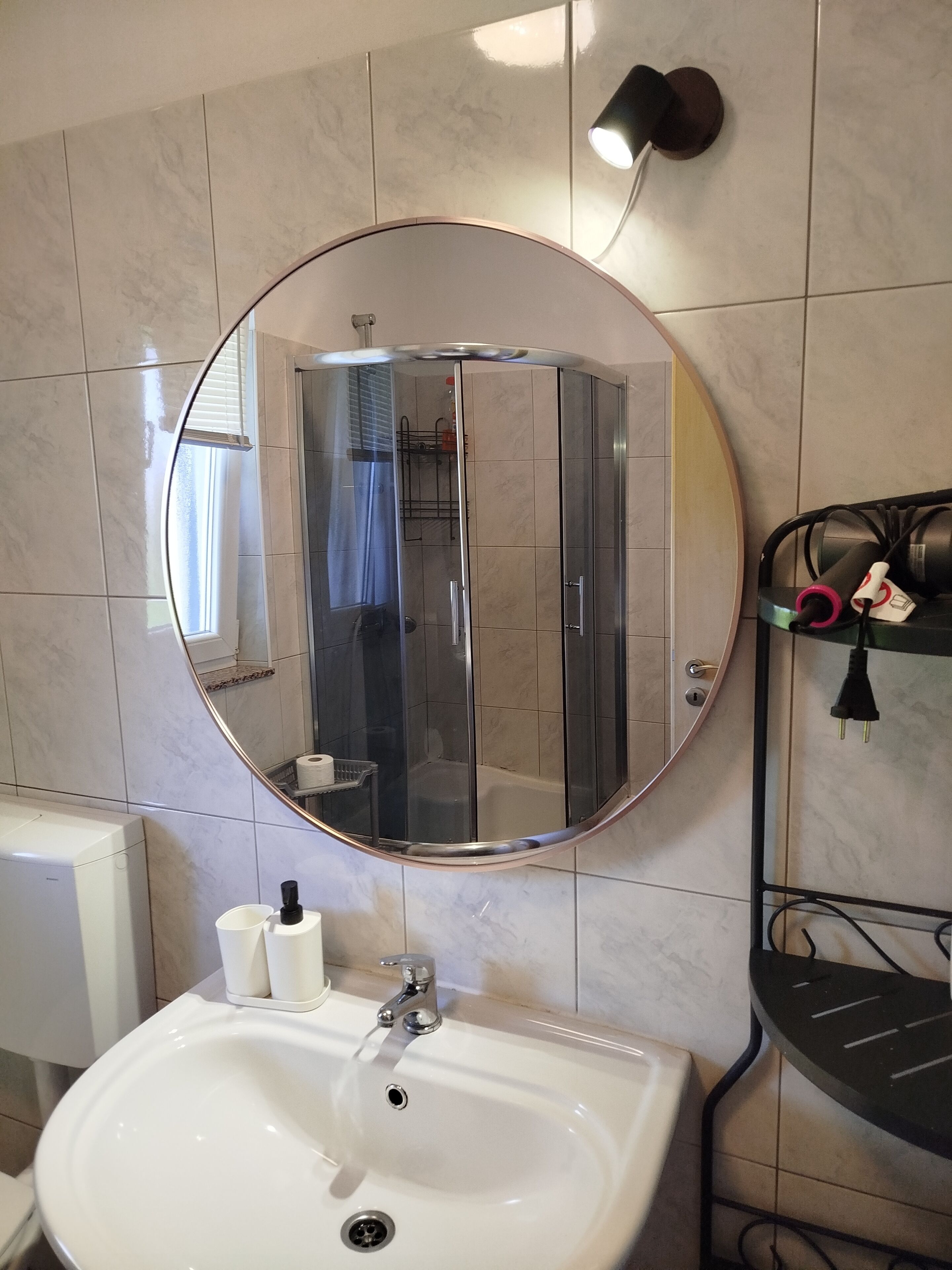 Une salle de bain avec un miroir rond, un lavabo, une douche et un porte-serviettes.