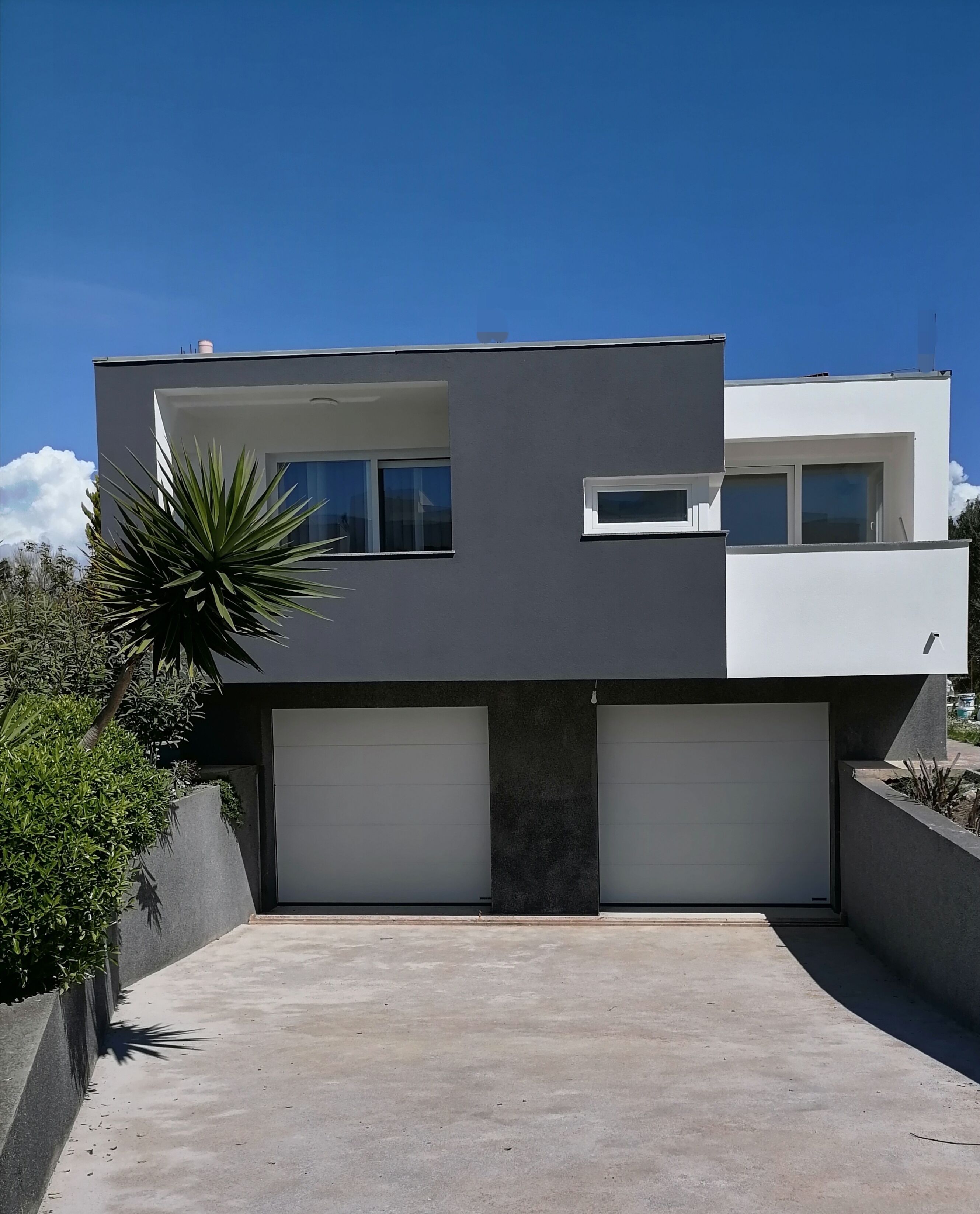 Una casa moderna de dos plantas con techo plano, ventanas grandes y entrada de hormigón.