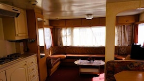 A compact RV interior with a kitchenette, a seating area with a sofa and a small table, and a window providing natural light. - Dutch House in Łazy near Lake Jamno (Łazy)