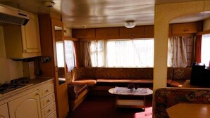 A compact RV interior with a kitchenette, a seating area with a sofa and a small table, and a window providing natural light. - Dutch House in Łazy near Lake Jamno (Łazy)
