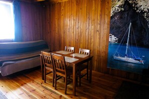 A wooden interior with a dining table and chairs, a sofa, and a mural of a sailboat on a cliff.