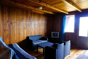 A wooden cabin interior with a sofa, a small table, and a television.