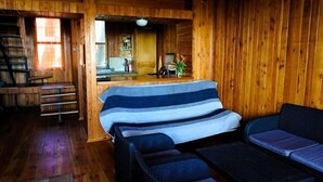 A wooden cabin interior with a bed, a sofa, a dining area, and a staircase. - Summer House in Łazy by Lake Jamno (Łazy)