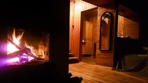 A cozy room with a fireplace, wooden walls, and a visible bathroom with a shower and toilet. - Summer House in Łazy by Lake Jamno (Łazy)