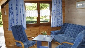 A wooden cabin with a blue-striped sofa, two armchairs, and a small table with a potted plant.