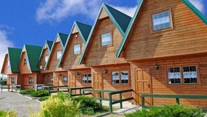 A row of wooden cabins with pitched roofs and green trim, arranged in a linear fashion.