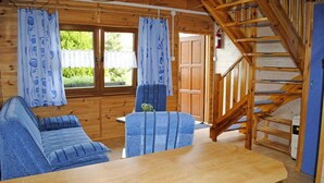 A wooden cabin interior with a sofa set, a dining table, and a staircase.