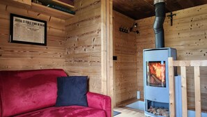 A cozy cabin interior with a red sofa, a framed newspaper, and a wood-burning stove.