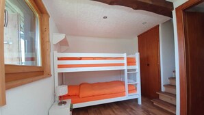 A bunk bed room with wooden flooring, a window, a lamp, and a door.