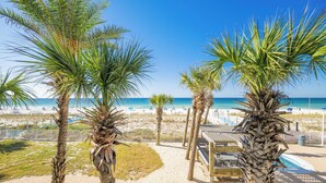Vista de la playa con palmeras, una piscina y una zona de terraza de madera.