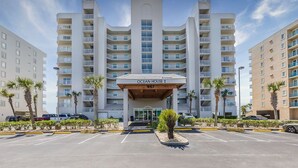 Un hotel de varios pisos con entrada central, balcones en cada planta y un estacionamiento al frente.