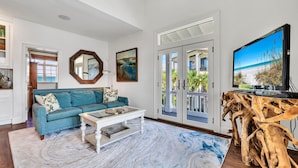 Un salon avec un canapé bleu, une table basse, un meuble TV en bois et une vue sur la plage, visible à travers des portes vitrées.