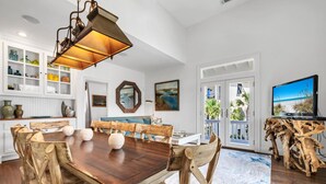 Un coin repas avec une table et des chaises en bois, un luminaire suspendu et une vue sur l’extérieur grâce à une porte vitrée.