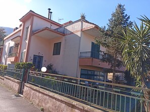 Two-story building with a flat roof and balcony, featuring a combination of exterior walls and a metal fence.