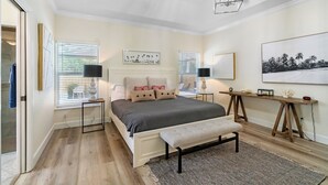 Un dormitorio con cama, mesitas de noche, un banco, un escritorio y obras de arte en las paredes.