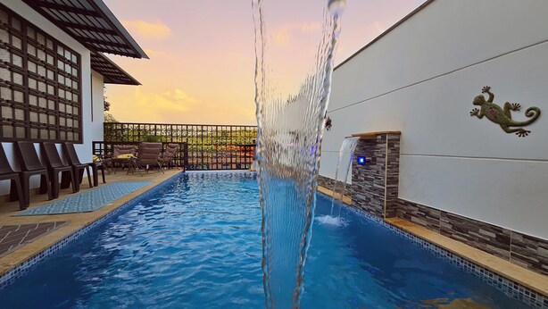 A swimming pool with a waterfall feature, surrounded by lounge chairs and a decorative wall.