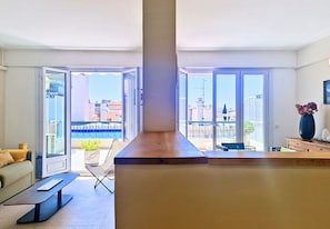 A modern living room with a large window, a sofa, a coffee table, and a wooden counter.