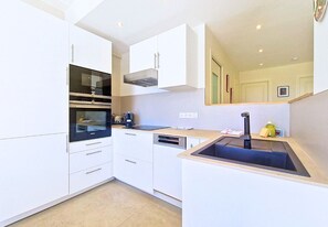 Una cucina compatta con mobili bianchi, forno integrato, lavastoviglie e lavello.
