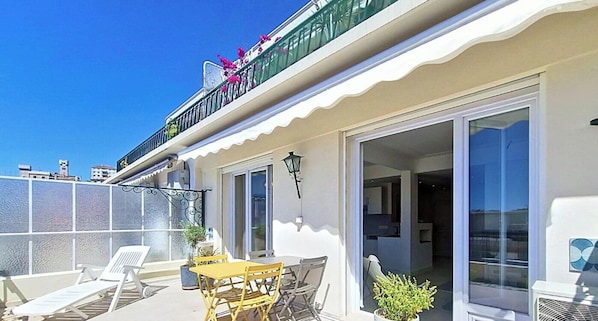 Ein Balkon mit Tisch und Stühlen, einem Blumentopf und Blick auf das Meer.
