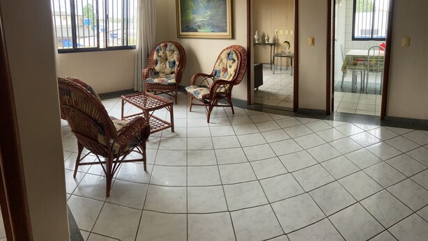 A spacious room with a tiled floor, two wicker chairs, a small table, and a painting on the wall. - AMORA SPACES - APARTAMENTO TOP LINHARES (Linhares)