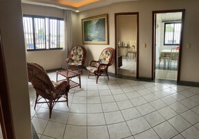 Um quarto amplo com piso de azulejos, duas cadeiras de vime, uma pequena mesa e um quadro na parede.