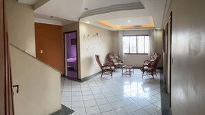 A spacious living area with a tiled floor, a staircase, and a seating area with wicker chairs and a small table. - AMORA SPACES - APARTAMENTO TOP LINHARES (Linhares)
