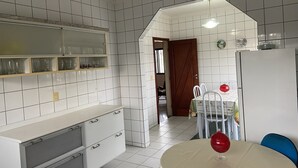 A kitchen with white tiled walls, a wooden door, a white refrigerator, and a dining table with chairs. - AMORA SPACES - APARTAMENTO TOP LINHARES (Linhares)