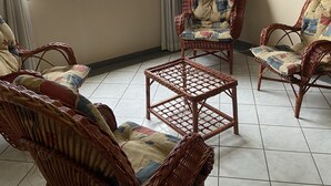 A room with wicker furniture, a painting, and a view of buildings through large windows. - AMORA SPACES - APARTAMENTO TOP LINHARES (Linhares)
