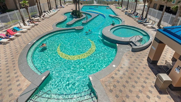 A pool area with multiple swimming pools, sun loungers, and palm trees. - Crystal Tower 1102 - Stunning Condo! (Gulf Shores)
